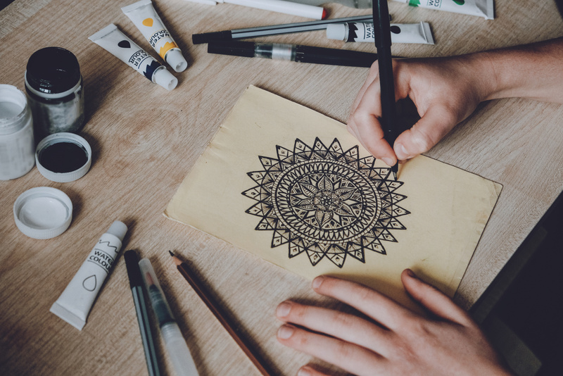 Hands Drawing a Mandala on Paper on Wooden Table